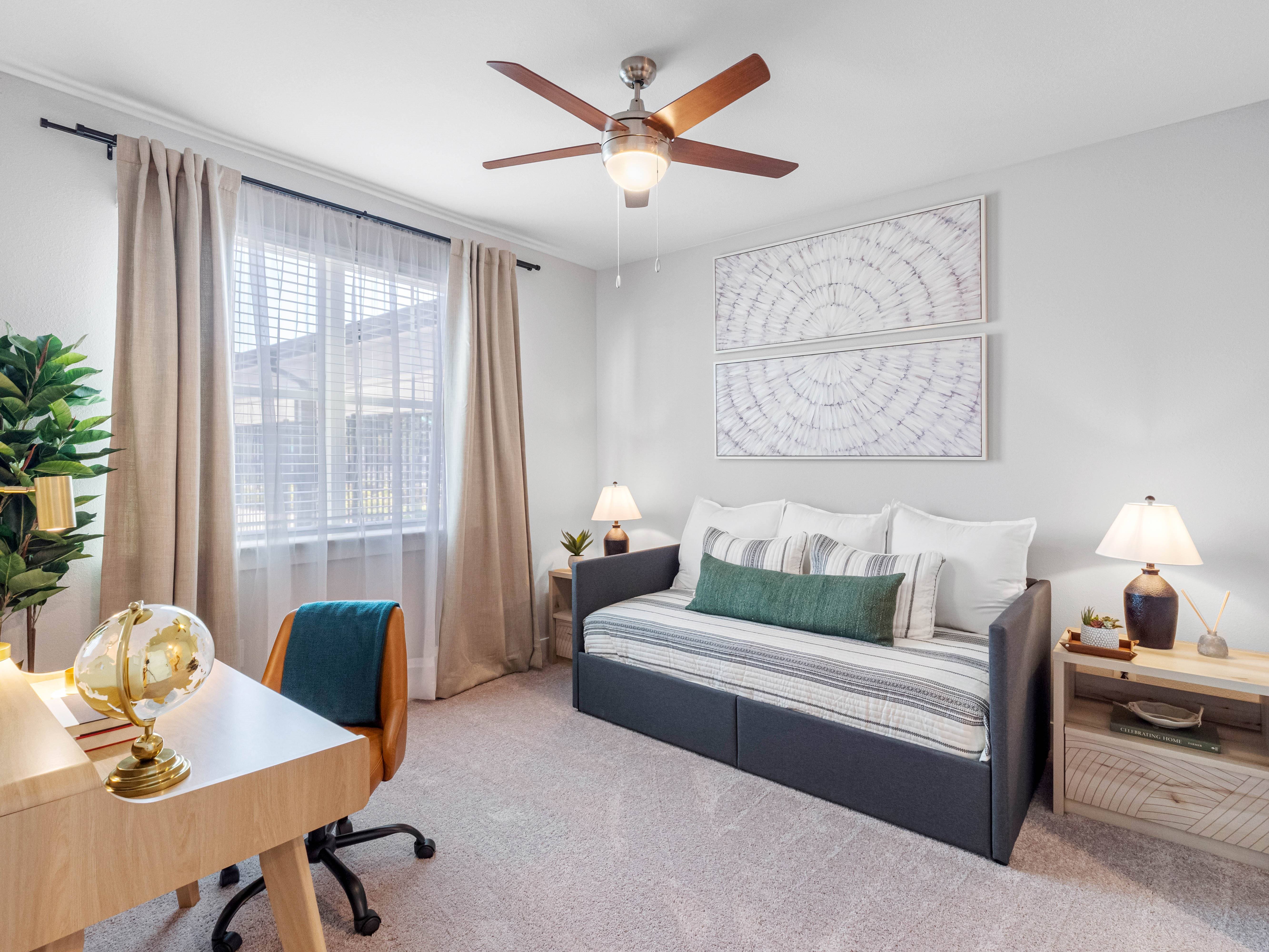A bedroom with a bed, a desk, and a ceiling fan.